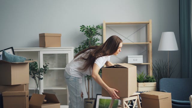 Person placing a cardboard box on a stool, with other cardboard boxes in the background